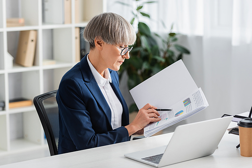 middle aged team leader in glasses holding folder with charts and graphs in office