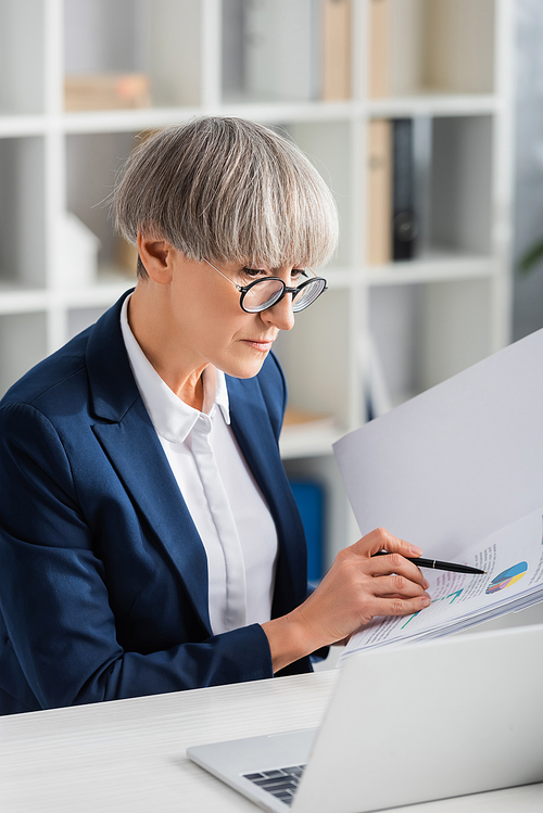 middle aged team leader in glasses holding folder with charts and graphs