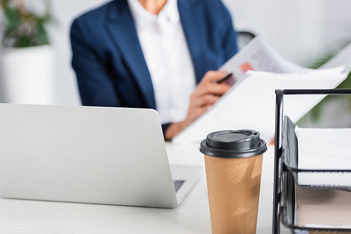 paper cup near laptop on desk with businesswoman on blurred background