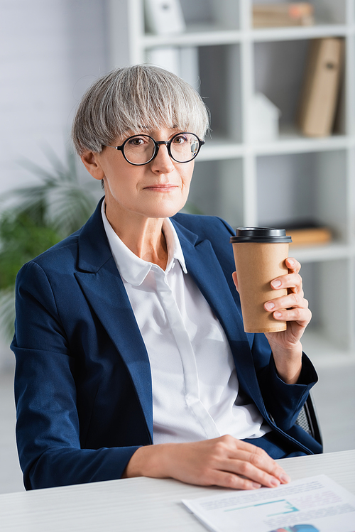 middle aged team leader in glasses holding paper cup with hot beverage in office