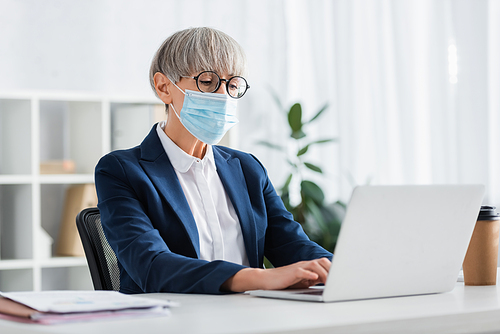 middle aged team leader in glasses and medical mask using laptop in office