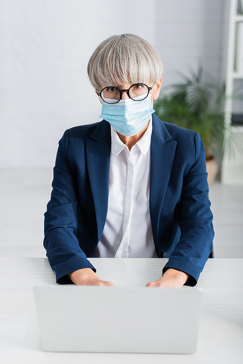 mature team leader in glasses and medical mask using laptop