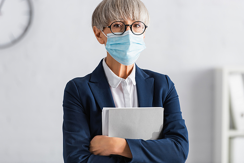 mature team leader in glasses and medical mask holding folder while