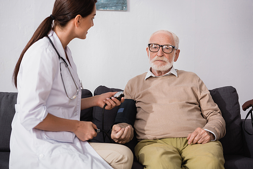 brunette geriatric nurse examining elderly man with stethoscope