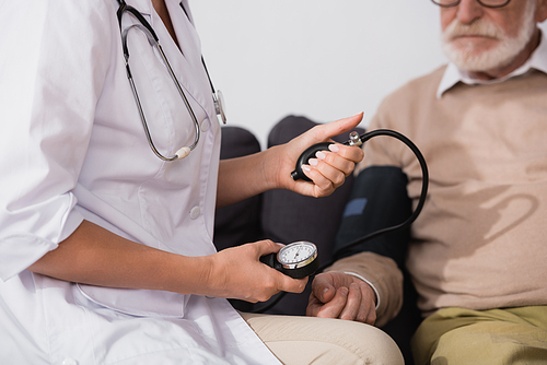 cropped view of geriatric nurse examining elderly patient with stethoscope on blurred background
