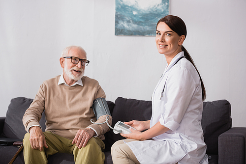 geriatric nurse examining aged man with tonometer at home