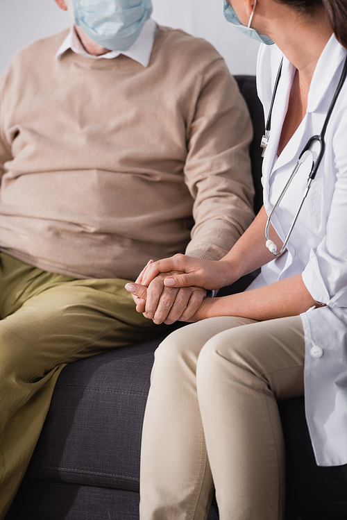 cropped view of nurse checking health by holding hands with aged patient