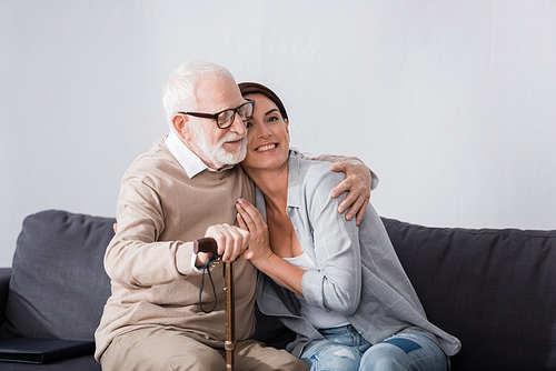 grateful elderly man hugging geriatric nurse while sitting on sofa at home