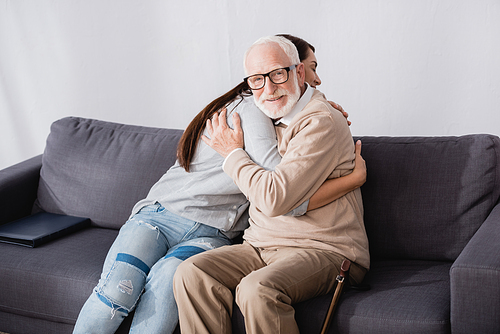 happy aged man  while sitting on sofa and embracing adult daughter