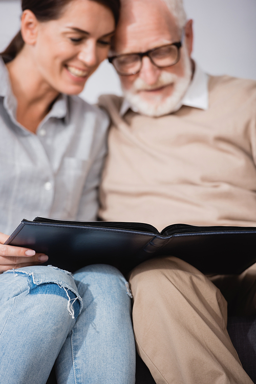 adult woman with elderly father browsing photo album on blurred background