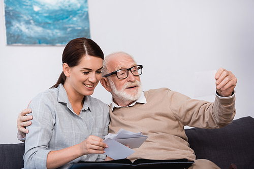 smiling woman with elderly father looking at family photos together at home