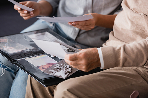 cropped view of aged father and adult daughter looking at family photos together on blurred background