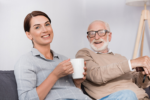 happy woman with cup of tea  while sitting near cheerful father