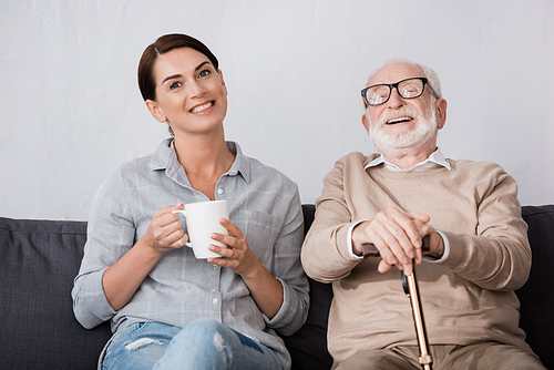 cheerful woman and laughing elderly father  while sitting on sofa