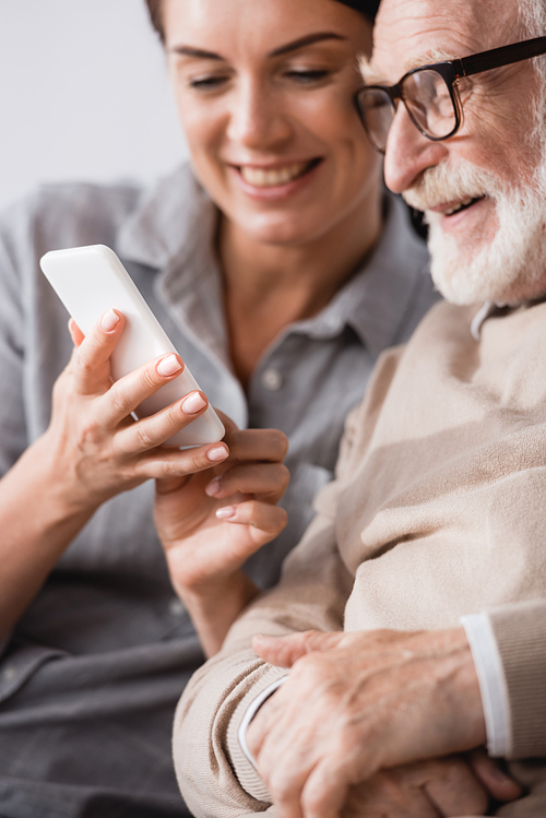 cheerful woman chatting on smartphone near happy dad on blurred background