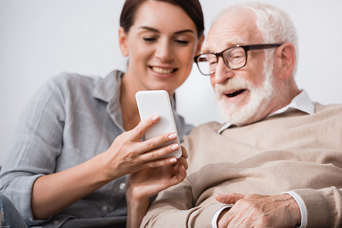 smiling woman showing mobile phone to cheerful aged father on blurred background