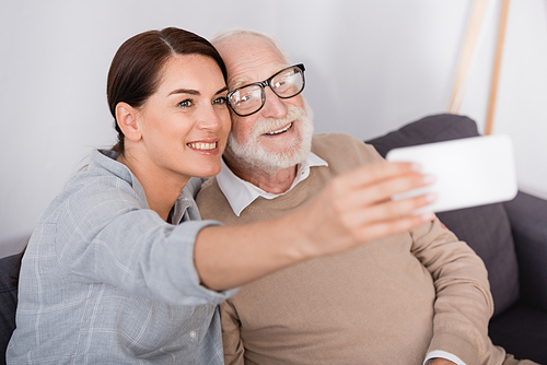 happy woman and senior man taking selfie on mobile phone on blurred foreground