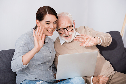 cheerful elderly man with daughter waving hands while having video chat on laptop