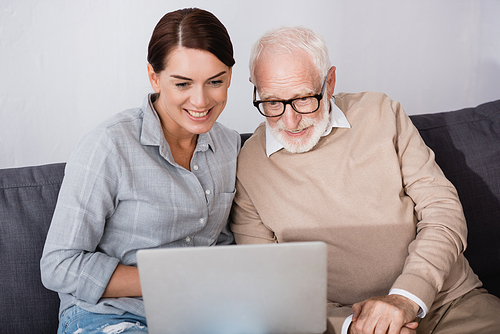 smiling woman with concentrated father using laptop together at home