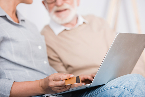 woman holding laptop and credit card near aged father on blurred background