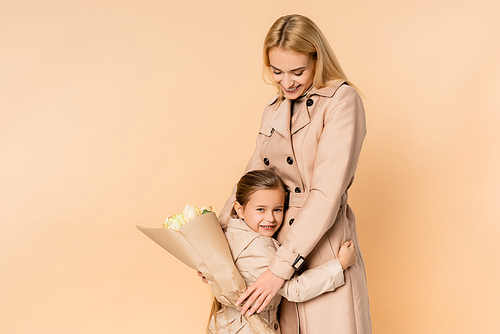 happy mother holding flowers and hugging cheerful daughter isolated on beige