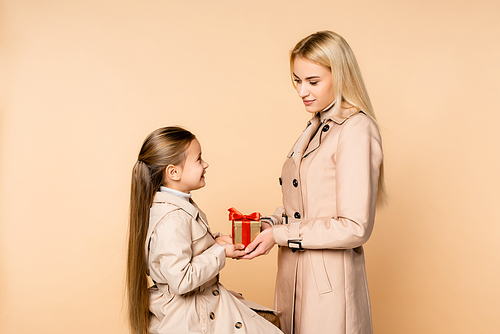cheerful kid giving present to happy mother on 8 march isolated on beige
