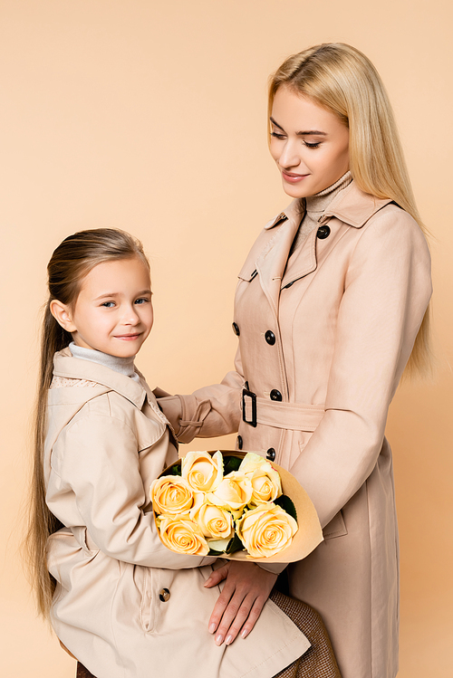 joyful kid holding roses near happy mother on 8 march isolated on beige
