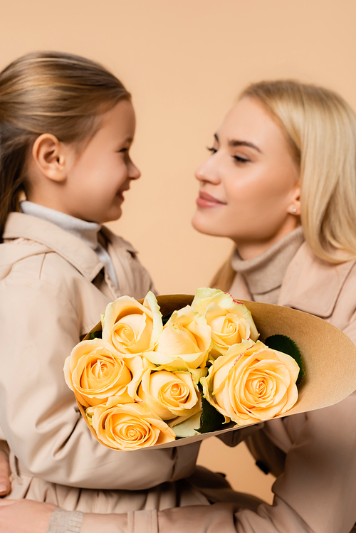 yellow roses in hands of kid near mother on 8 march and blurred background isolated on beige