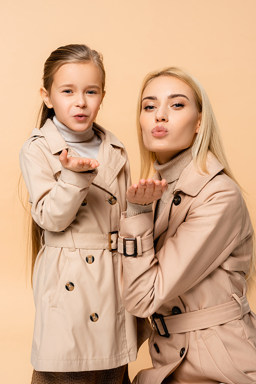 mother and daughter in trench coats sending air kisses isolated on beige