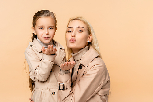 mother and daughter in coats sending air kisses isolated on beige