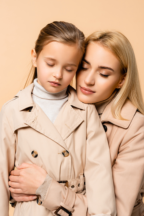 caring mother and daughter with closed eyes hugging isolated on beige