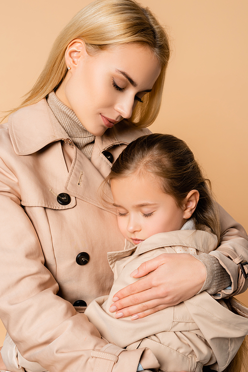 blonde mother embracing daughter with closed eyes isolated on beige