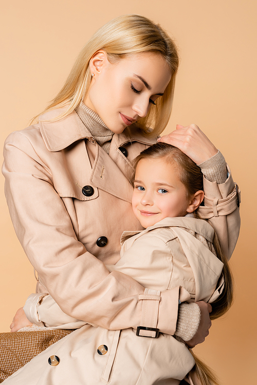 caring and blonde mother embracing daughter isolated on beige