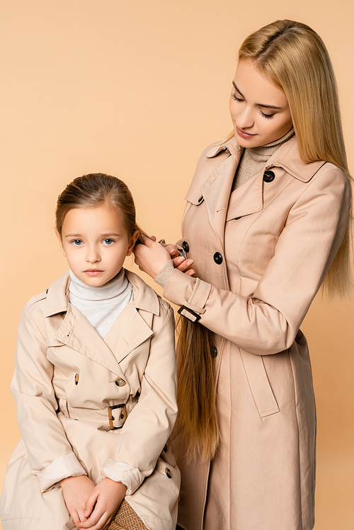 blonde mother weaving braid on daughter isolated on beige