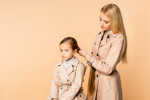 caring mother weaving braid on daughter isolated on beige