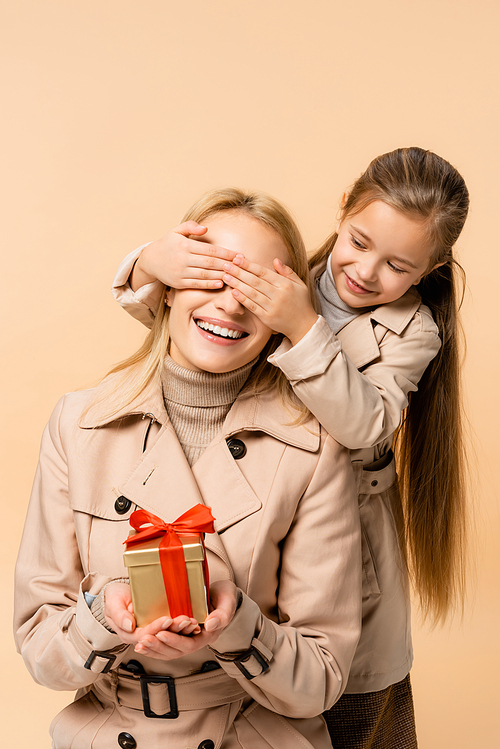 kid covering eyes of happy mother with present isolated on beige