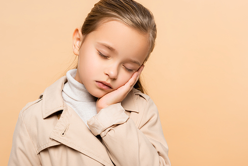 sleepy kid with closed eyes in trench coat isolated on beige