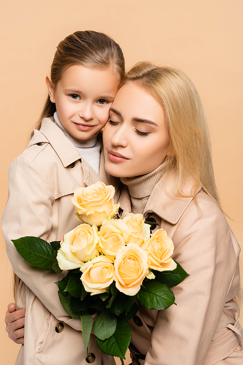 mother holding flowers and hugging daughter isolated on beige