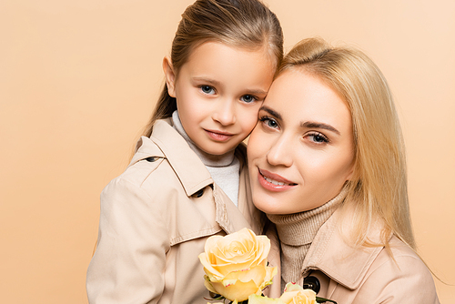 joyful mother holding flowers and hugging daughter isolated on beige