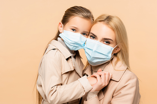 mother and daughter in medical masks holding hands isolated on beige