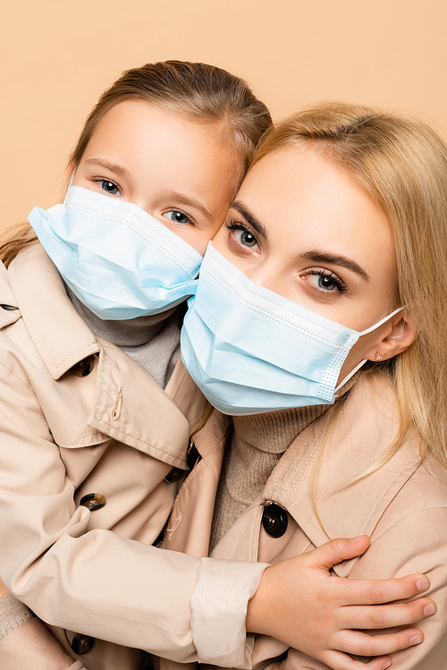 mother and daughter in medical masks  isolated on beige