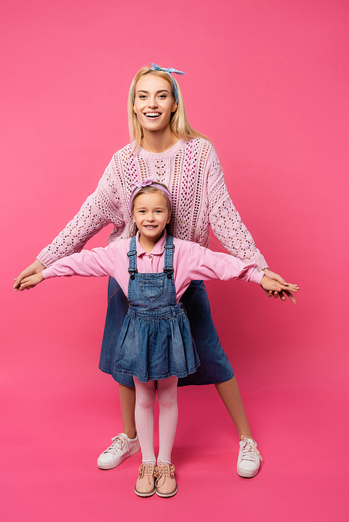 full length of mother and kid smiling and standing with outstretched hands isolated on pink