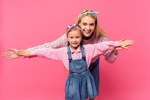 happy mother and kid smiling while standing with outstretched hands isolated on pink