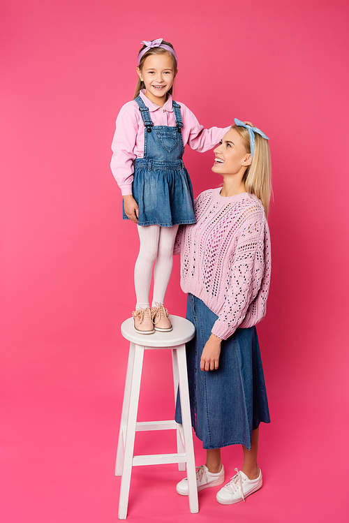 happy kid standing on chair near smiling mother on pink