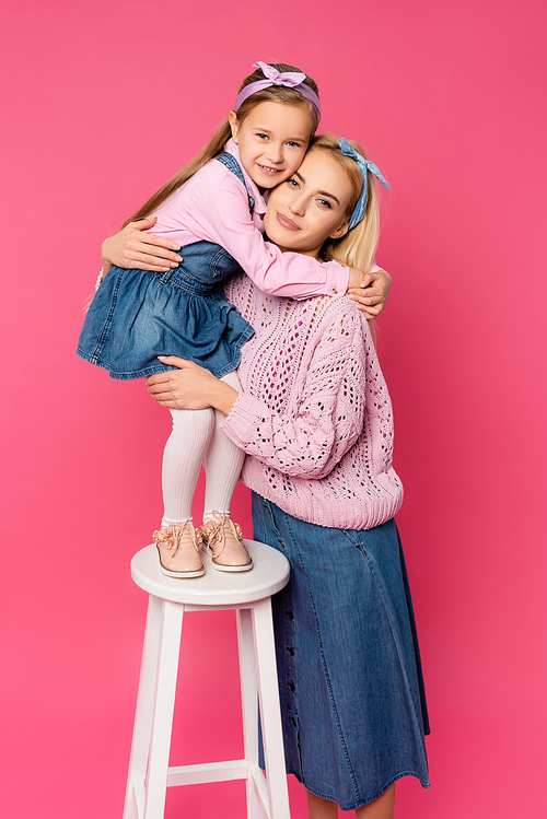 happy kid standing on chair and hugging mother on pink