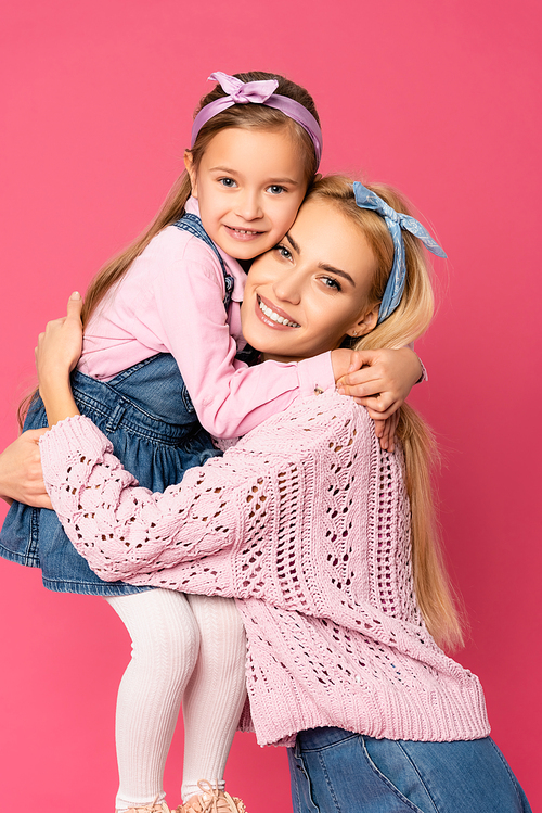 happy daughter smiling while hugging mother isolated on pink