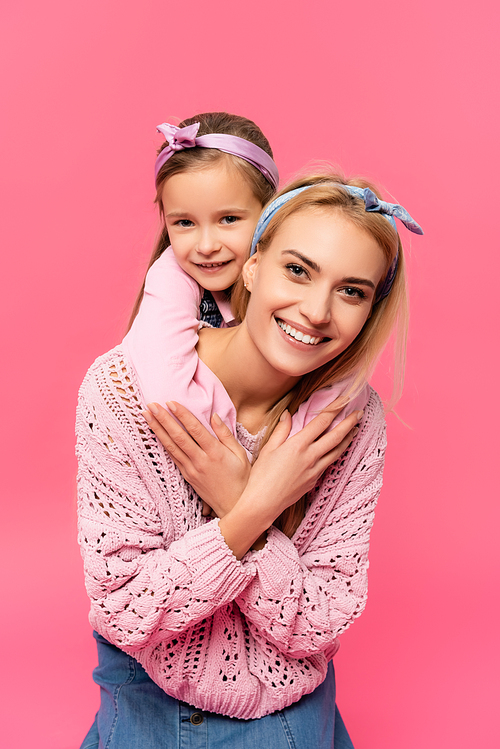 cheerful kid hugging happy mother isolated on pink