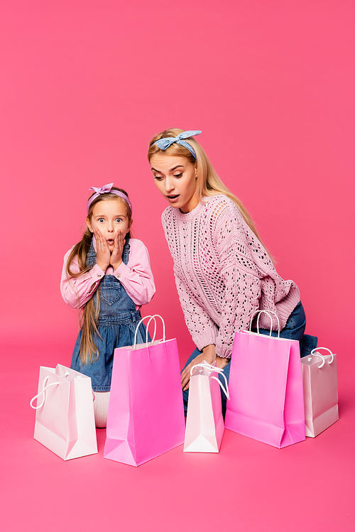 shocked mother and daughter looking at shopping bags on pink