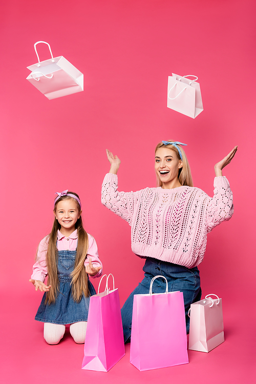 amazed mother and daughter smiling near shopping bags on pink