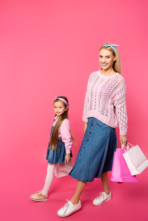happy mother and daughter walking with shopping bags on pink